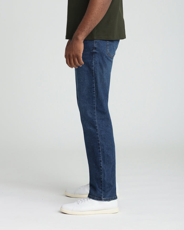 Man wearing medium blue denim jeans with relaxed fit and olive green t-shirt.
