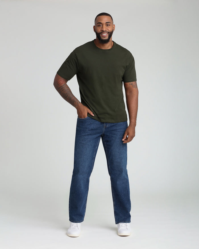 Man wearing olive green short-sleeve crewneck t-shirt with medium blue straight-leg jeans and white sneakers.