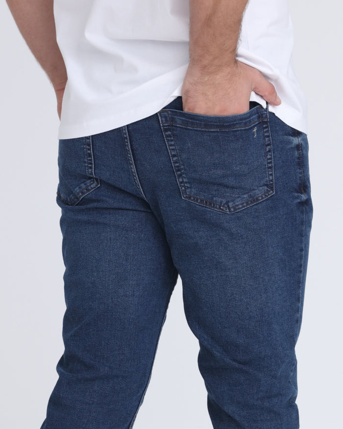 Man wearing medium blue denim jeans with relaxed fit and white t-shirt, back pocket detail visible.