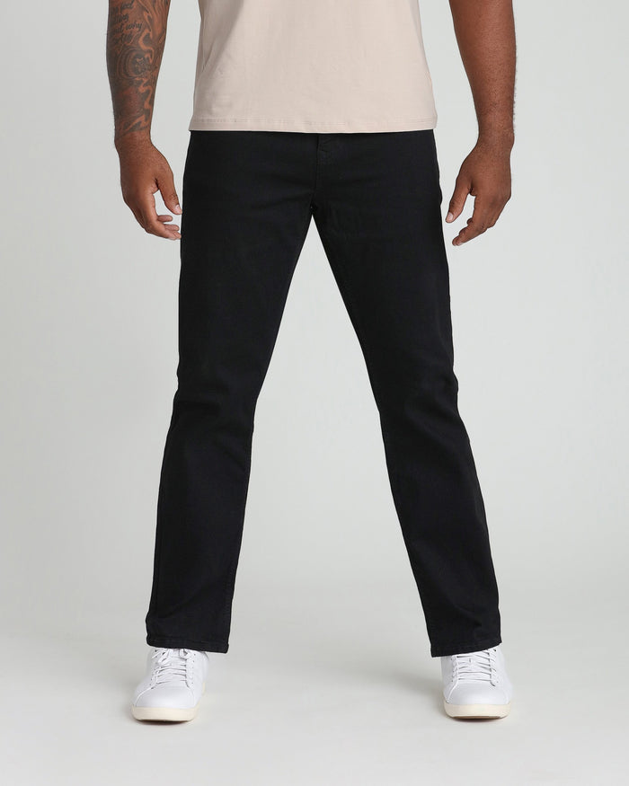 Man wearing black jeans with a relaxed fit and white sneakers paired with a cream-colored t-shirt.