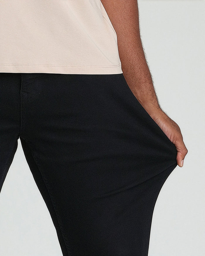 Black pants with relaxed thigh fit and tapered leg, shown with cream-colored top.