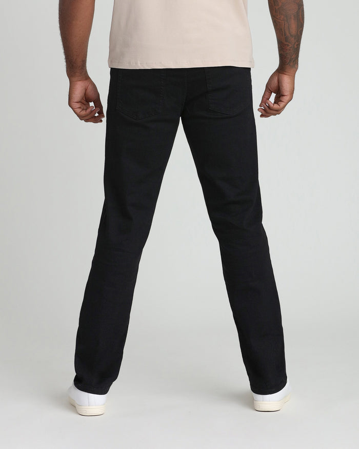 Man wearing black straight-leg jeans with cream t-shirt and white sneakers, shown from behind.