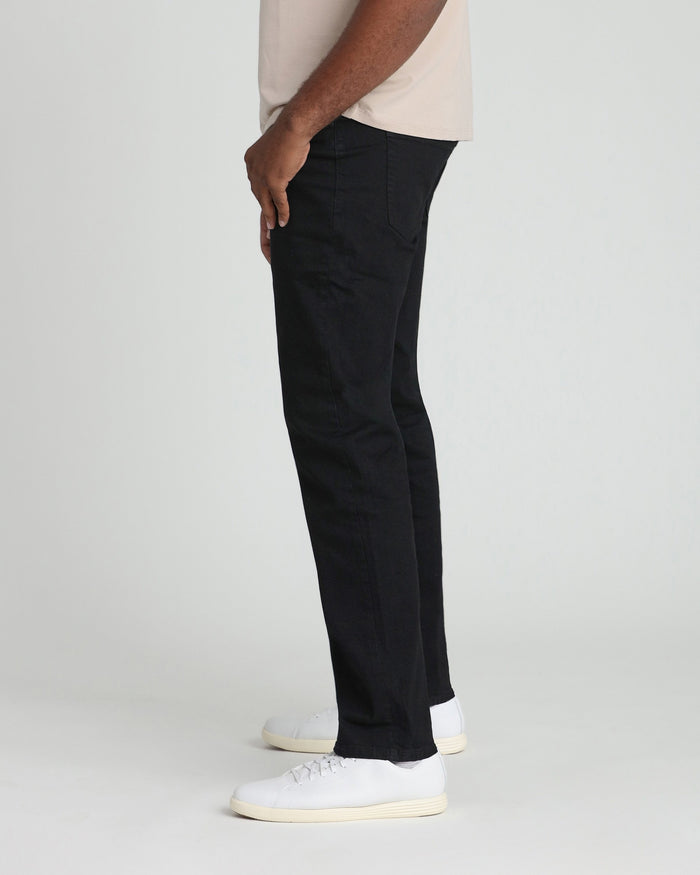 Black jeans with relaxed thigh fit and tapered leg on model wearing cream sneakers.