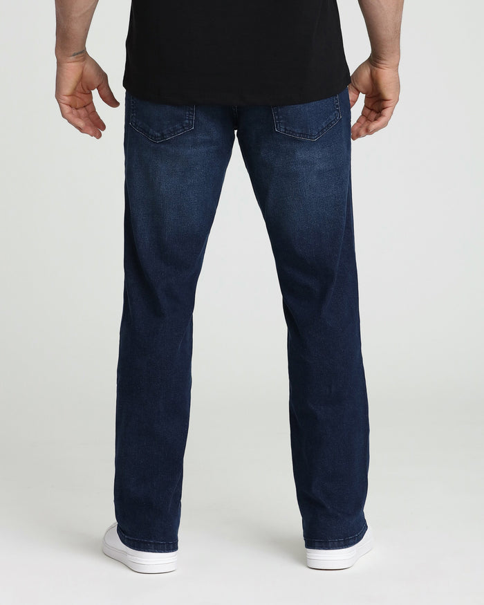 Rear view of midnight blue straight-leg jeans with pocket stitching detail on model wearing black shirt and white sneakers.