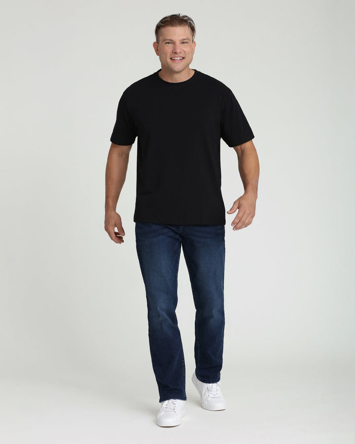 Man wearing black crew neck t-shirt with dark blue jeans and white sneakers.