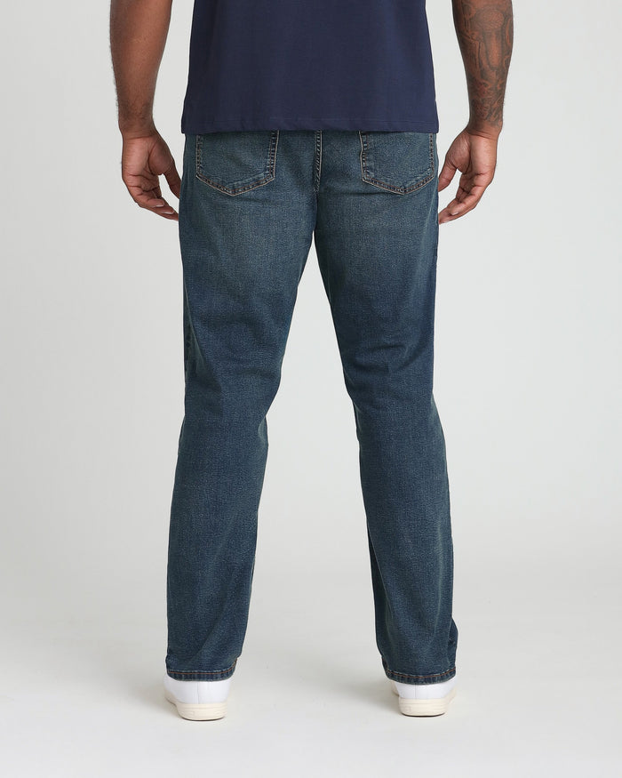 Man wearing dark blue t-shirt and tinted blue denim jeans with white sneakers, back view.