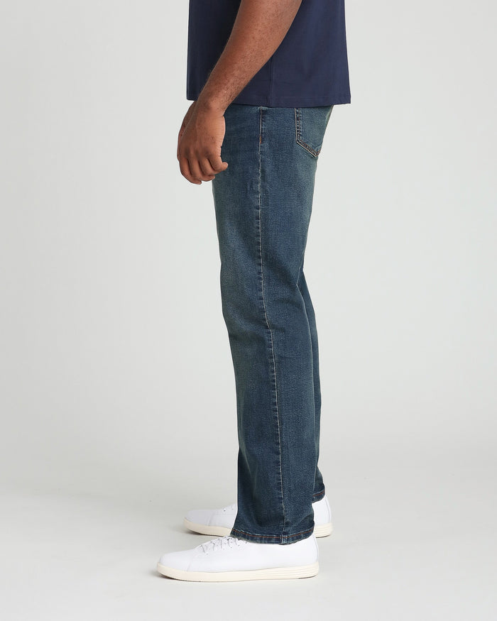 Man wearing dark blue t-shirt and tinted dark denim jeans with white sneakers, side view.