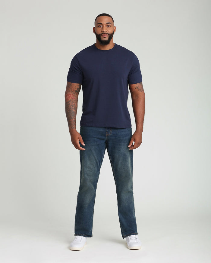 Man wearing navy crew neck t-shirt and medium-wash straight-leg jeans with white sneakers.