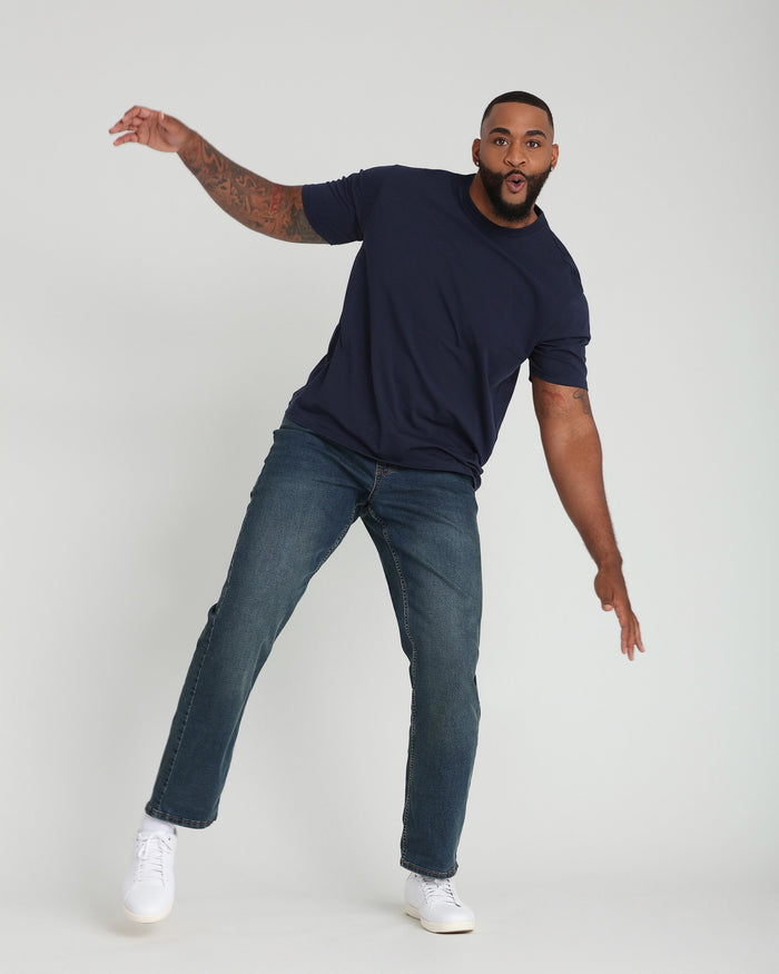 Man wearing navy short-sleeve t-shirt, medium-wash straight-leg jeans, and white sneakers.
