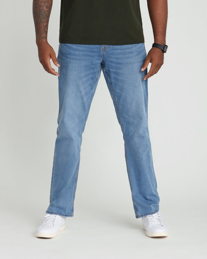 Light indigo bootcut jeans on model wearing olive green shirt and white sneakers.