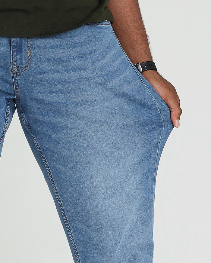 Light indigo denim jeans with relaxed fit shown on model wearing olive shirt.