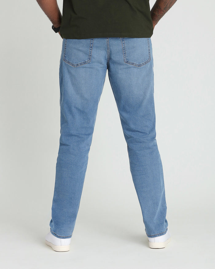 Light indigo jeans with relaxed fit, worn with olive green shirt and white sneakers, shown from back.