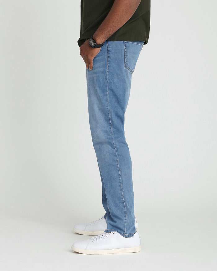 Man wearing light indigo denim jeans with a relaxed fit and white sneakers.