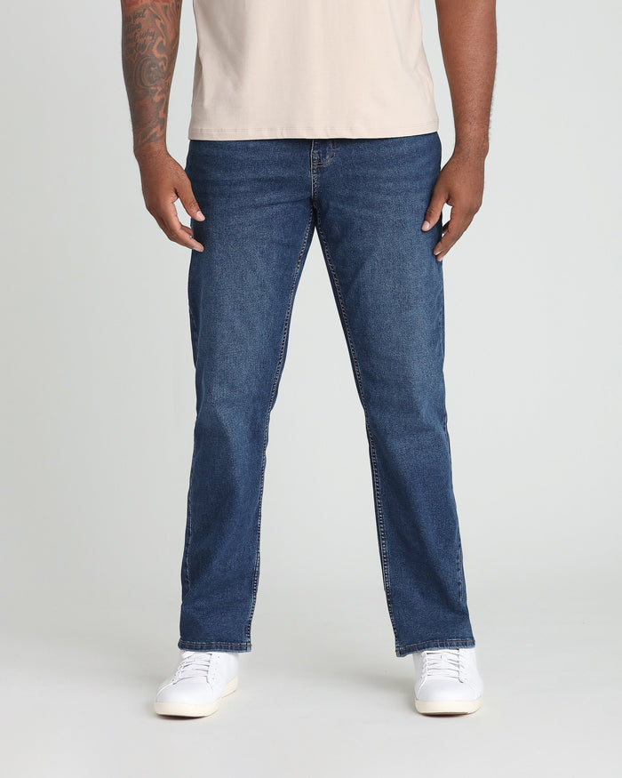 Man wearing dark blue straight-fit jeans with cream t-shirt and white sneakers.