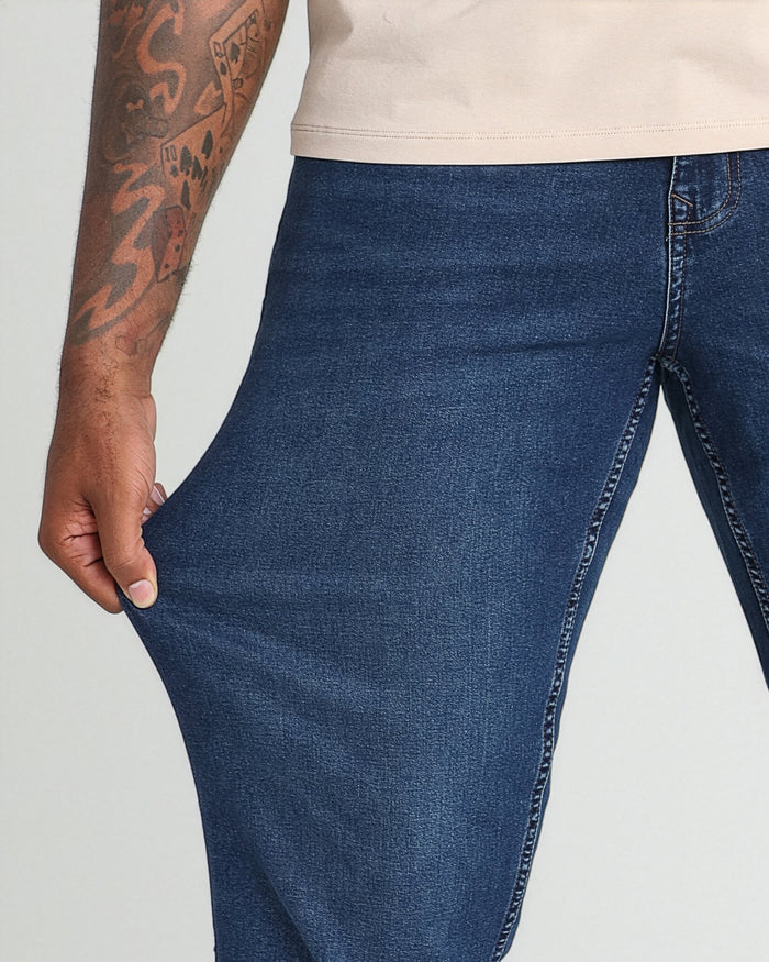 Man wearing dark blue denim jeans with cream t-shirt, showing thigh and waistband detail.