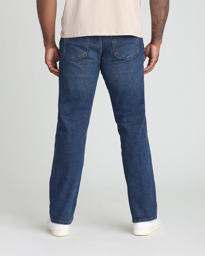 Man wearing cream t-shirt and dark blue denim jeans, shown from back view.