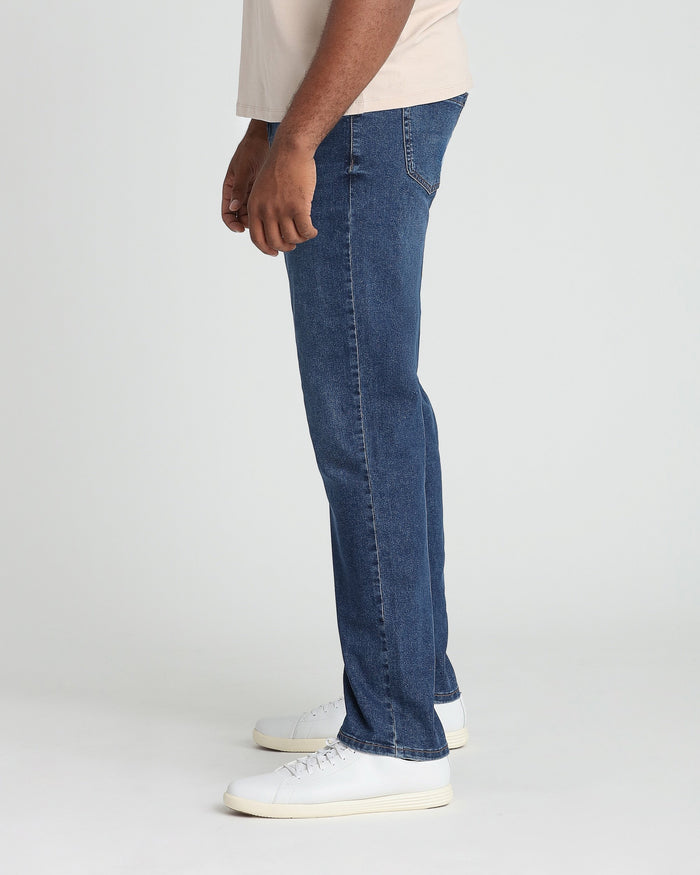 Dark blue denim jeans with relaxed fit, shown on model wearing cream sneakers and light-colored shirt.