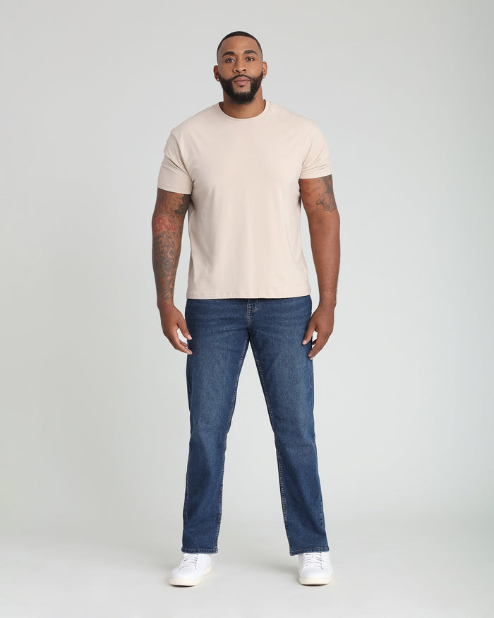 Man wearing cream crew neck t-shirt and dark blue jeans with white sneakers.