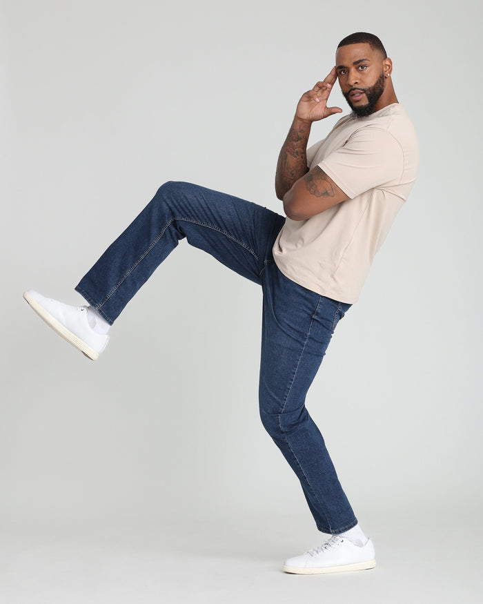 Man wearing dark blue jeans with cream t-shirt and white sneakers.