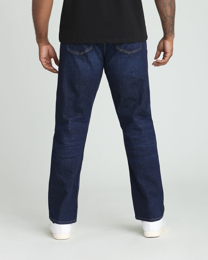 Man wearing dark blue jeans with black shirt and white sneakers, shown from behind.