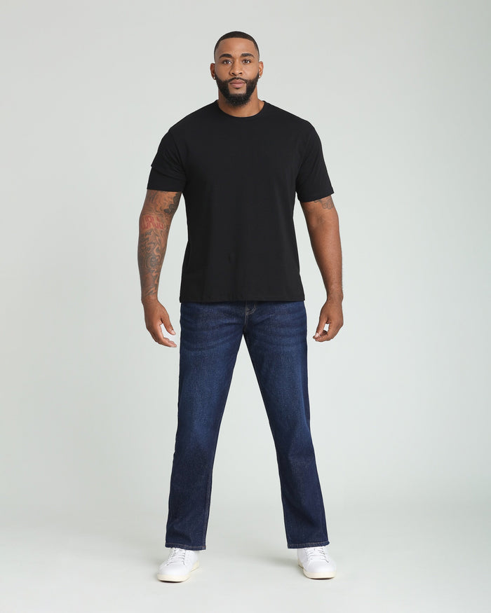 Man wearing black short-sleeve crewneck t-shirt and dark blue jeans with white sneakers.