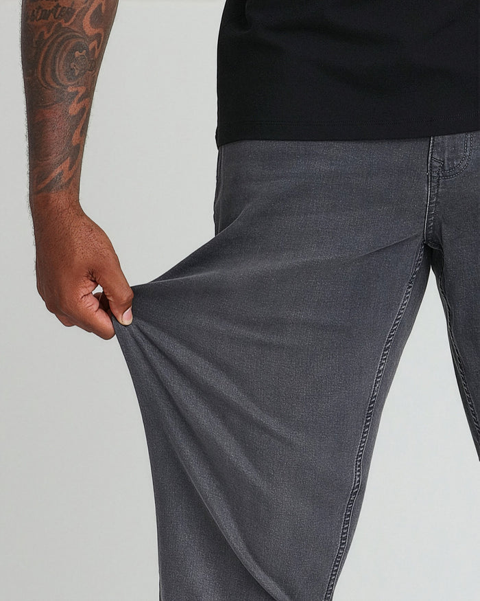 Grey denim jeans with relaxed fit, shown on model wearing black shirt, hand pulling at thigh fabric.