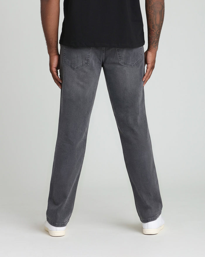 Man wearing black t-shirt and grey denim jeans with white sneakers, shown from behind.