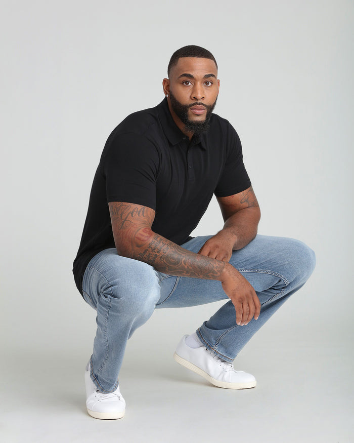 Man wearing black polo shirt and light blue jeans with white sneakers in crouching pose.