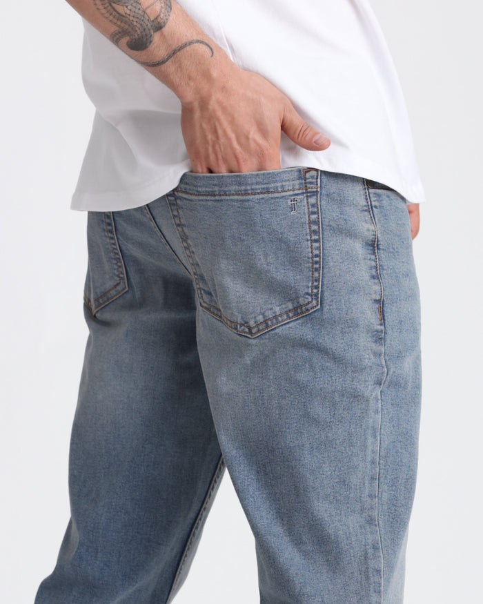 Light blue denim jeans with relaxed fit, visible back pocket and stitching details, worn with white shirt.