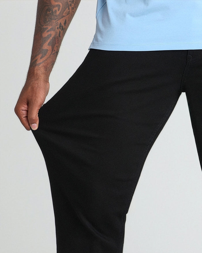 Black tapered pants with relaxed thigh fit, paired with light blue t-shirt on tattooed model.