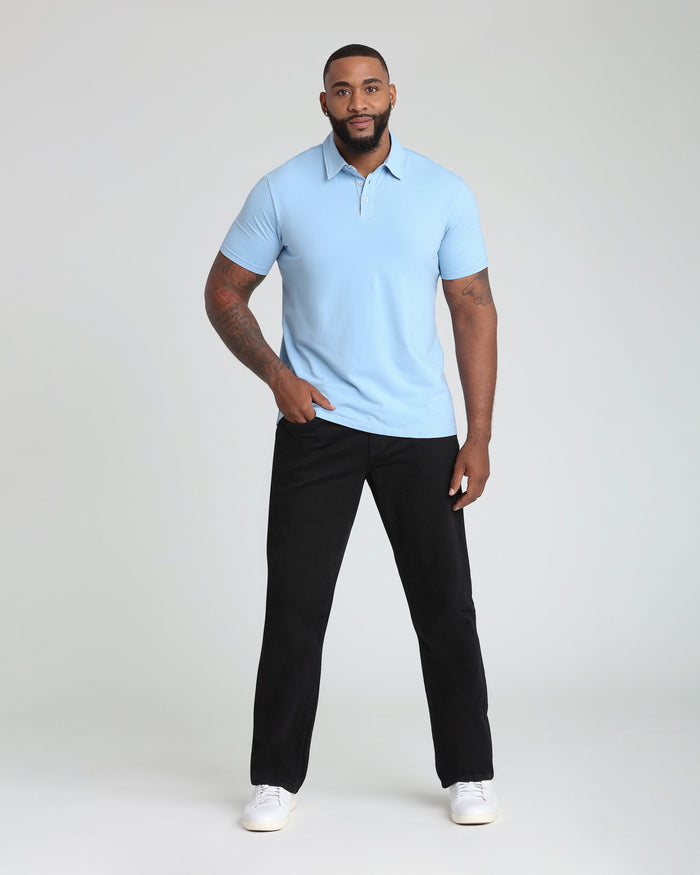Man wearing light blue short-sleeve polo shirt with collar and black pants with white sneakers.