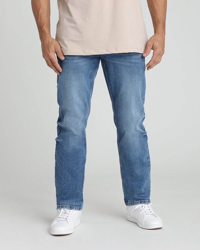 Man wearing medium blue denim jeans with relaxed fit and white sneakers.