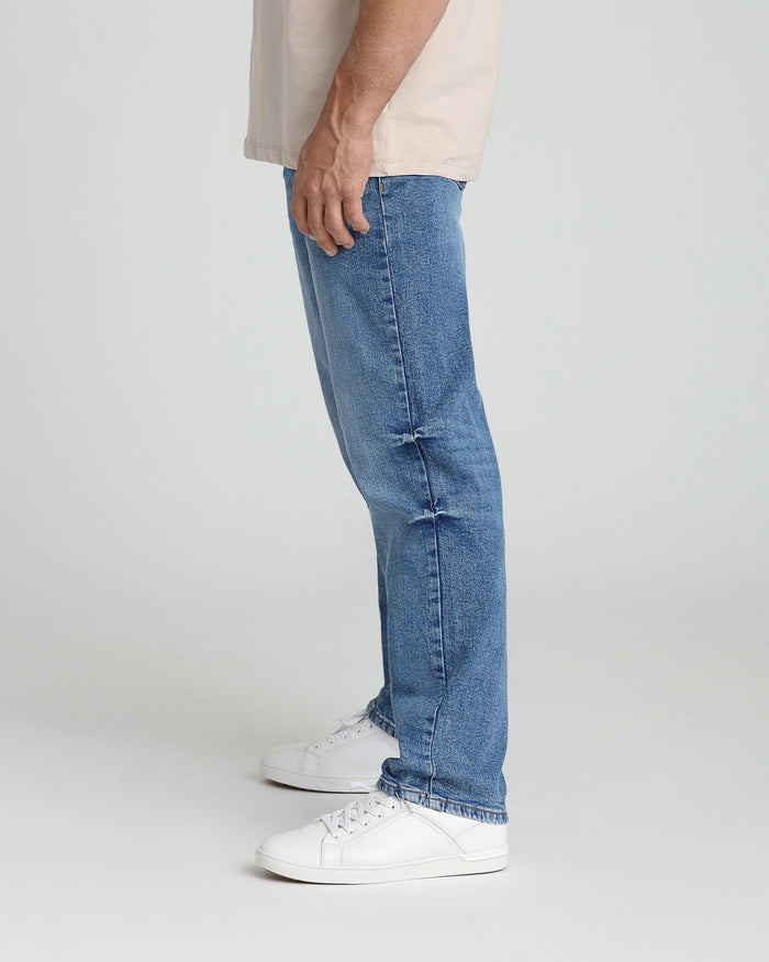 Medium blue relaxed-fit jeans with straight leg and frayed hem, shown on model wearing white sneakers.