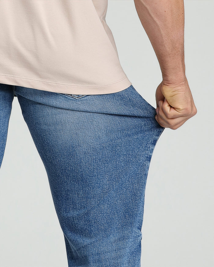 Medium blue denim jeans with relaxed fit worn with cream-colored long-sleeve shirt.