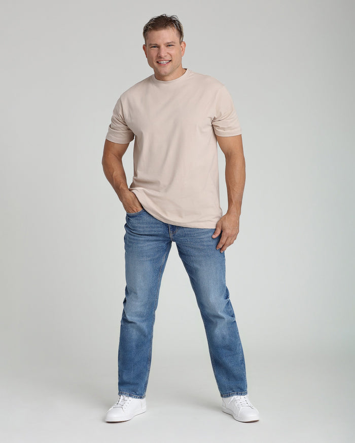 Man wearing beige short-sleeve t-shirt and medium blue jeans with white sneakers.