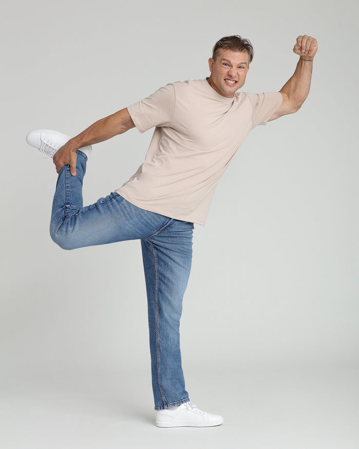 Man wearing cream-colored short-sleeve t-shirt and medium blue jeans with white sneakers.