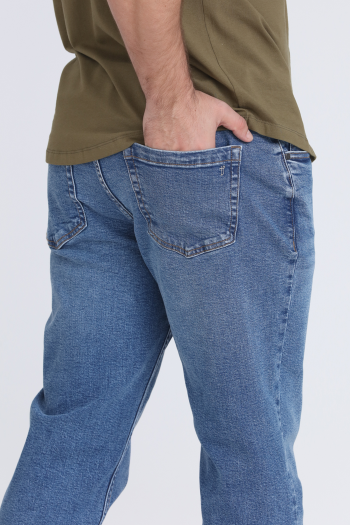 Medium blue jeans with relaxed fit, visible rear pockets, and contrast stitching worn with olive-colored shirt.