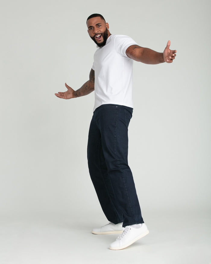 Man wearing white t-shirt and deep blue relaxed-fit jeans with white sneakers.