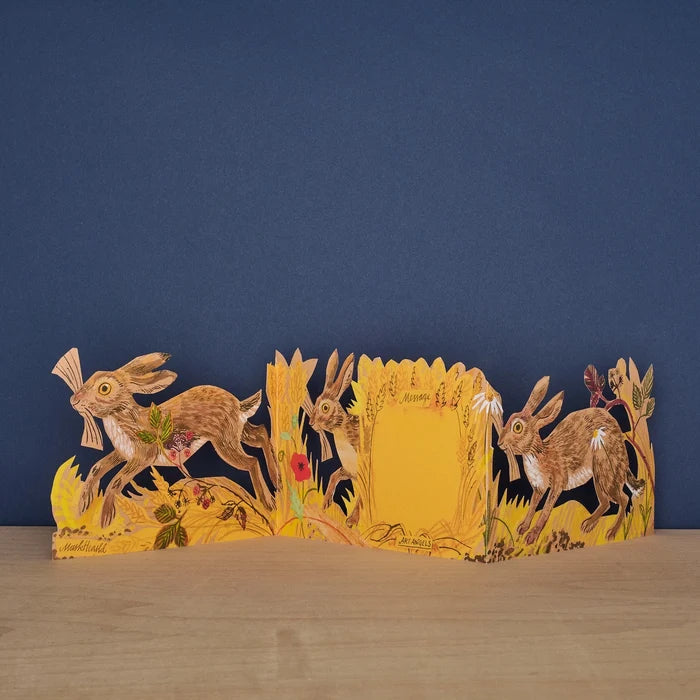 Hares Collage concertina card open to reveal blank message panel, with illustrated hares and meadow botanicals on either side, signed by Mark Hearld and Art Angels
