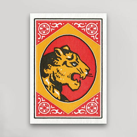 A post card featuring a stylized roaring tiger head in yellow and black on a red circular background, framed by a yellow and red decorative border with white ornamental motifs, shown against a light gray wall.