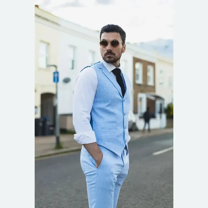 Male model in a light blue linen suit with waistcoat and trousers, white shirt, black tie, sunglasses, standing outdoors