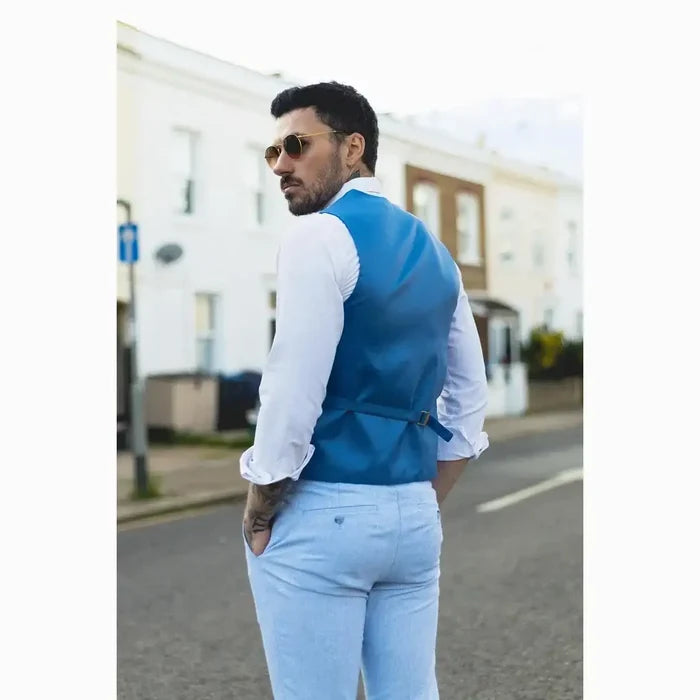 Male model in a light blue linen suit with waistcoat, white shirt, black tie, sunglasses, posing outdoors on street