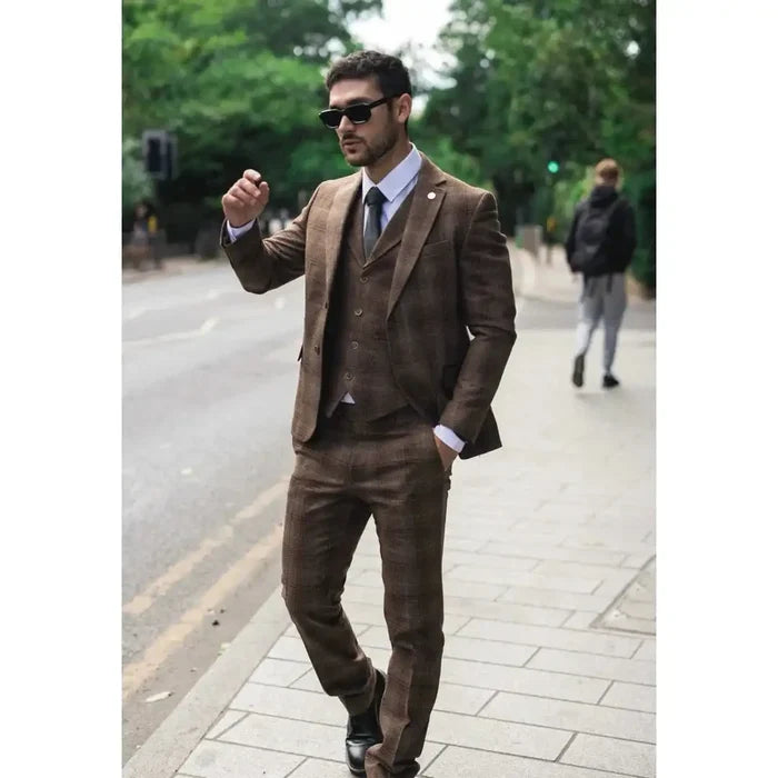 Man wearing a brown tweed check suit with matching blazer, waistcoat, and trousers, accessorized with sunglasses, white shirt, and dark tie