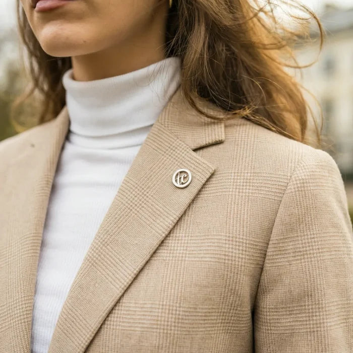 Close-up of beige women's tailored suit with check pattern, notched lapel, and a decorative pin on the blazer's collar