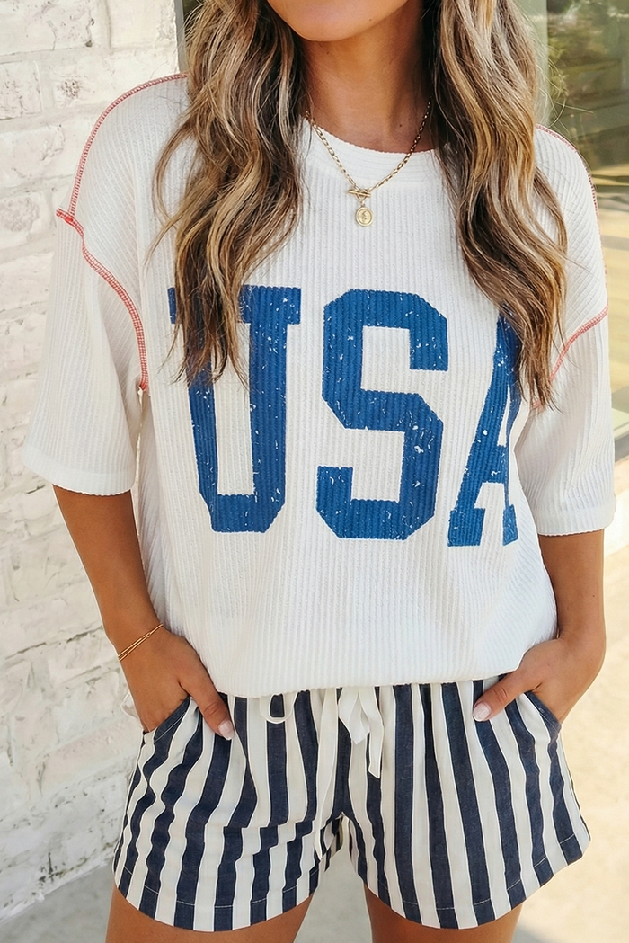 Person wearing a white 'USA' t-shirt and striped shorts against a blurred background