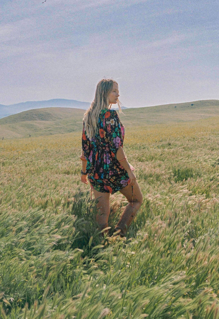 Model wearing Valley of the Dolls Boho Blouse in Onyx, back view showing waist ties in grassy field