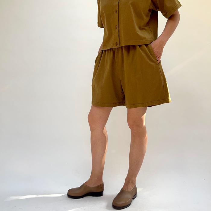 Person wearing brown cotton shorts, brown top and shoes against a white background