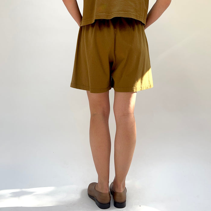 Person wearing a brown outfit with shorts and a top on a white background, viewed from the back